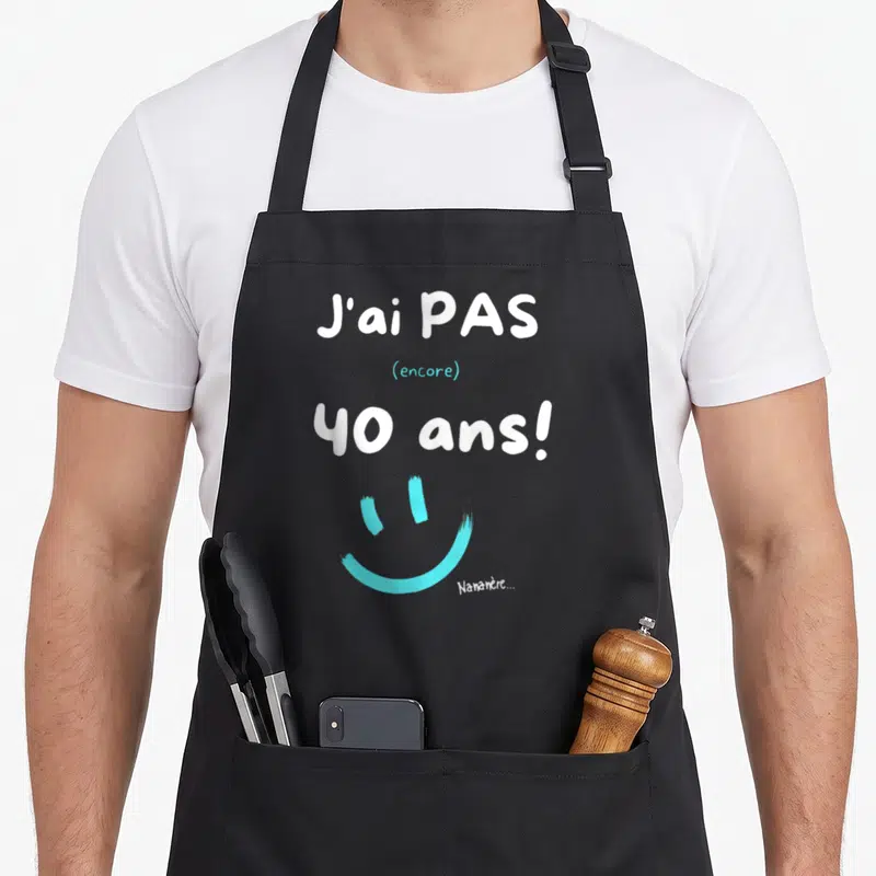 Tablier de cuisine noir avec l'inscription J'ai pas encore 40 ans et un grand smiley turquoise sous le texte.