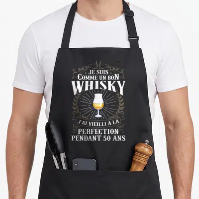 Tablier de cuisine noir avec illustration de verre à whisky et texte blanc sur fond gris uni