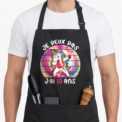 Tablier de cuisine noir avec licorne colorée effectuant un dab sur fond tie-dye circulaire.