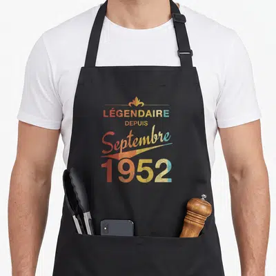 Tablier de cuisine noir avec inscription Légendaire Depuis Septembre 1952 en lettres colorées et style vintage délavé.