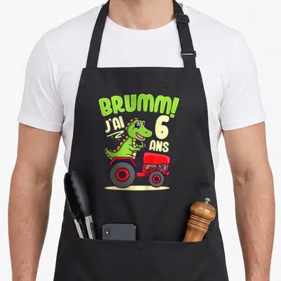 Tablier de cuisine noir avec dinosaure vert au volant d'un tracteur rouge et texte J'ai 6 ans Brumm