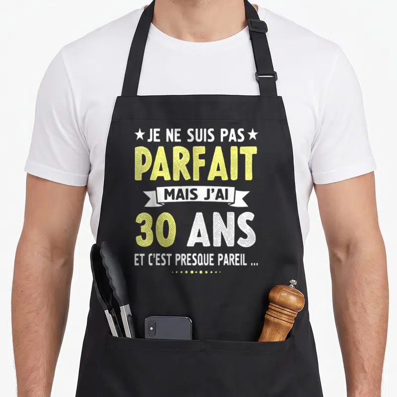 Tablier de cuisine noir avec le texte Je ne suis pas parfait mais j'ai 30 ans en typographie jaune et blanche.