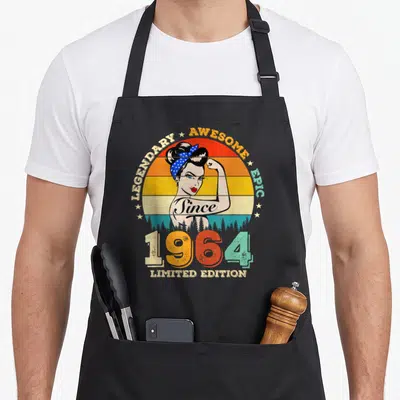 Tablier de cuisine noir avec illustration vintage d'une femme musclée et texte Since 1964 Limited Edition coloré.