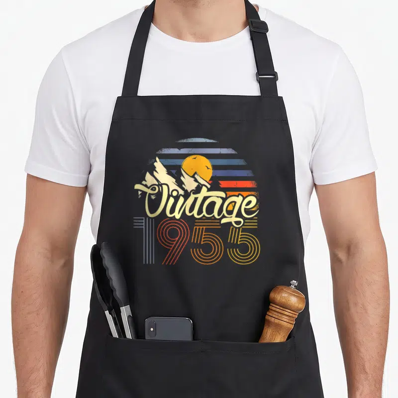 Tablier de cuisine noir avec motif vintage 1955 représentant un soleil couchant sur des montagnes en style rétro.