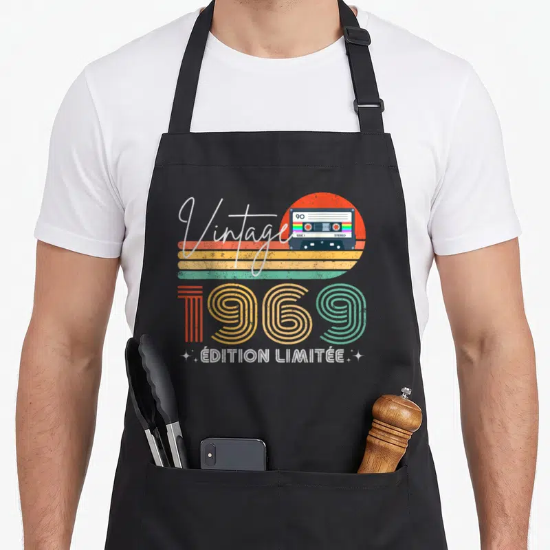 Tablier de cuisine noir avec illustration vintage 1969, cassette audio et soleil coloré rétro.