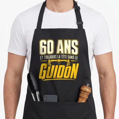 Tablier de cuisine noir avec inscription 60 ans et toujours la tête dans le guidon en jaune et blanc sur fond uni.