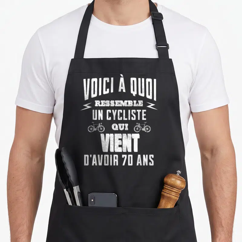 Tablier de cuisine noir avec inscription voici à quoi ressemble un cycliste qui vient d'avoir 70 ans et deux bicyclettes blanches.