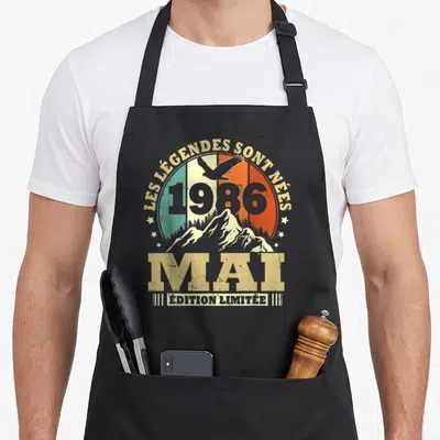 Tablier de cuisine noir avec motif vintage Les Légendes sont Nées en Mai 1986 illustrant un aigle au-dessus de montagnes.