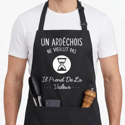 Tablier de cuisine noir avec texte blanc Un Ardèchois ne vieillit pas et icône sablier.