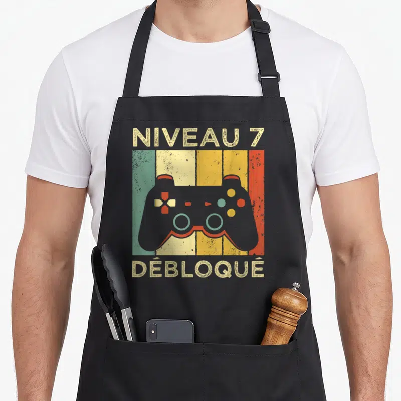 Tablier de cuisine noir avec illustration manette de jeu vidéo et texte Niveau 7 Débloqué en style rétro.
