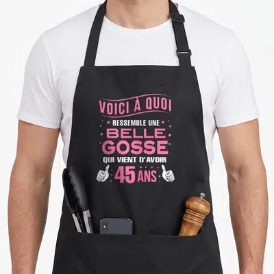 Tablier de cuisine noir avec inscription rose et blanche célébrant les 45 ans d'une belle gosse encadrée de deux pouces levés.