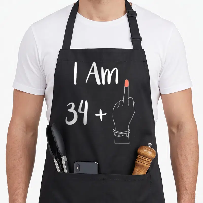 Tablier de cuisine noir avec l'inscription I Am 34 plus une main levant le majeur en rouge.