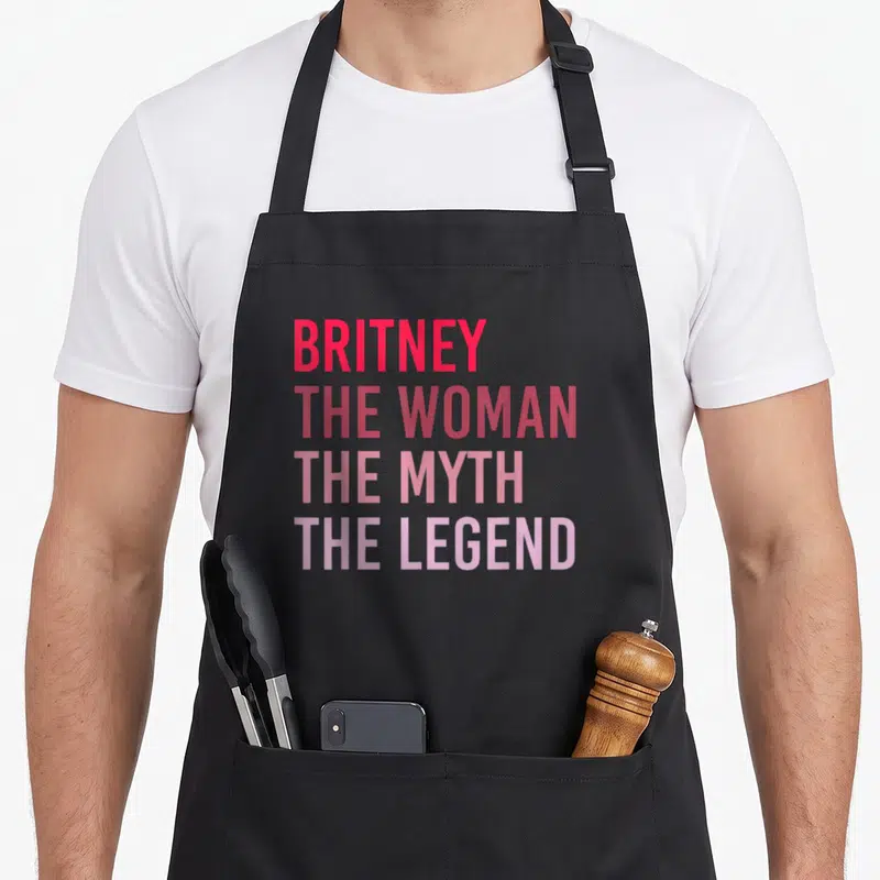 Tablier de cuisine noir avec le texte BRITNEY THE WOMAN THE MYTH THE LEGEND en dégradé rose et rouge.