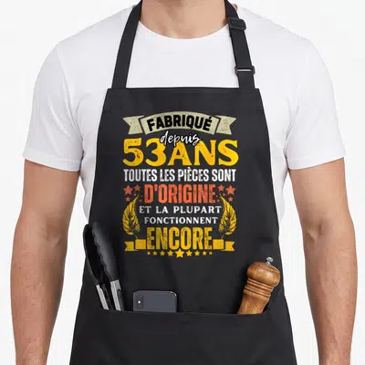 Tablier de cuisine noir avec inscription colorée célébrant les 53 ans et les pièces d'origine.