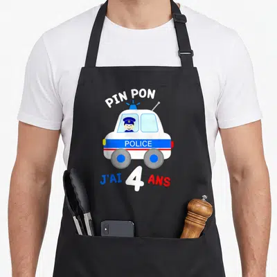Tablier de cuisine noir avec voiture de police blanche, texte pin pon et j'ai 4 ans en couleurs vives.