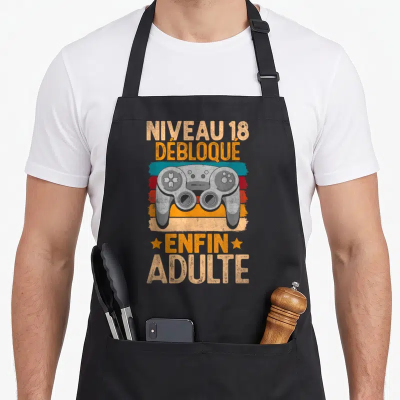 Tablier de cuisine noir avec illustration de manette de jeu et texte Niveau 18 Débloqué Enfin Adulte sur fond coloré vintage.