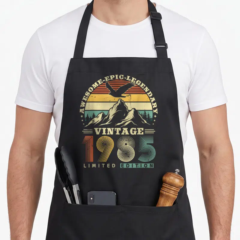 Tablier de cuisine noir avec motif rétro 1985 montrant un aigle au-dessus de montagnes colorées.