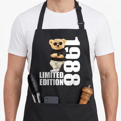 Tablier de cuisine noir avec ours aux lunettes de soleil, bras croisés et texte 1988 Limited Edition imprimé en blanc.