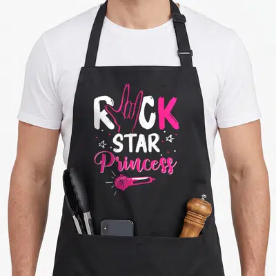 Tablier de cuisine noir avec l'inscription Rock Star Princess et un micro rose vif au centre.