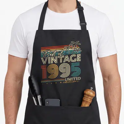 Tablier de cuisine noir avec illustration vintage Best of Vintage 1995 Limited Edition et palmiers en arrière-plan de bandes colorées.