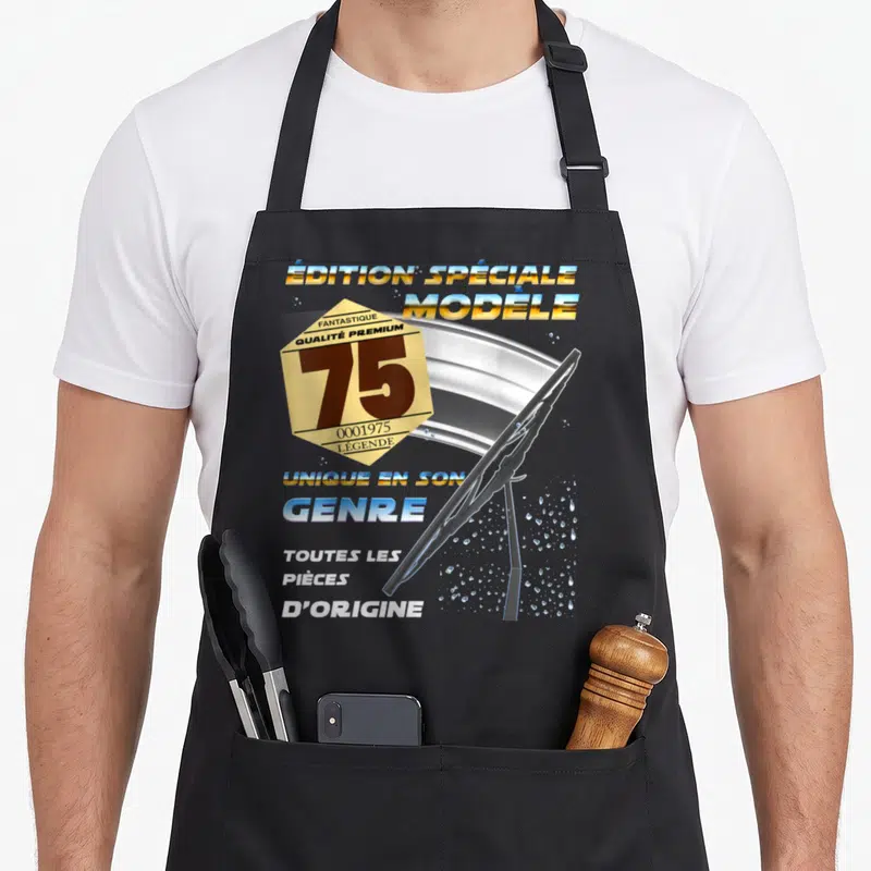 Tablier de cuisine noir avec illustration de balai de windshield et badge doré affichant le nombre 75 ainsi que des textes sur le motif.
