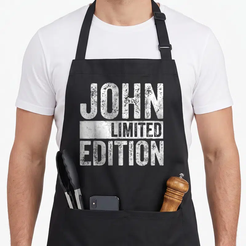 Tablier de cuisine noir avec inscription blanche John Limited Edition en typographie distressed et effet usé sur le devant.