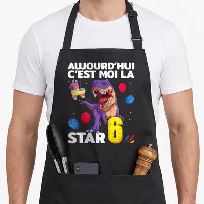 Tablier de cuisine noir avec un dinosaure violet, une piñata colorée et le chiffre 6 doré pixelisé.