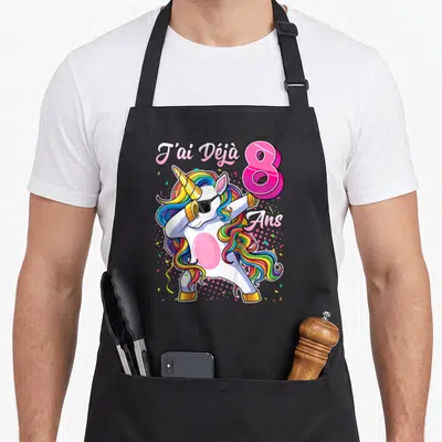 Tablier de cuisine noir avec une licorne aux cheveux multicolores effectuant un mouvement dab sous le texte J'ai déjà 8 ans.