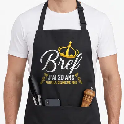 Tablier de cuisine noir avec inscription Bref j'ai 20 ans pour la deuxième fois et une couronne dorée.
