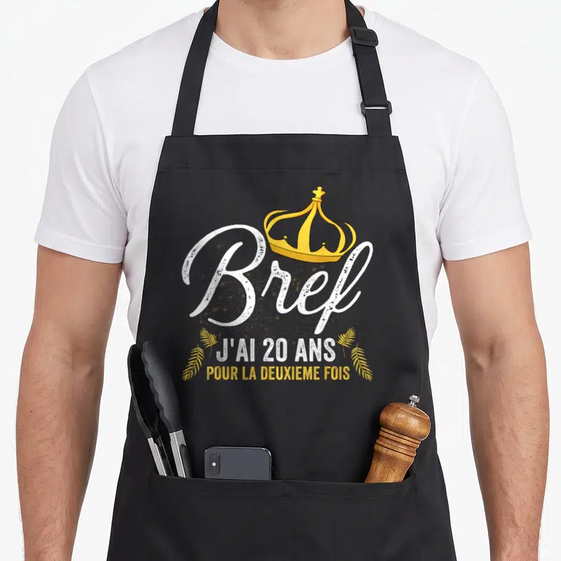 Tablier de cuisine noir avec inscription Bref j'ai 20 ans pour la deuxième fois et une couronne dorée.