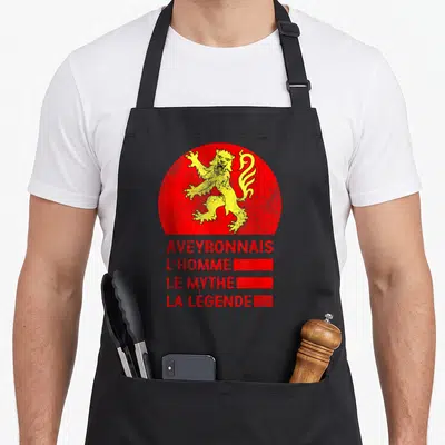 Tablier de cuisine noir avec un lion jaune stylisé sur fond rouge circulaire et du texte en rouge