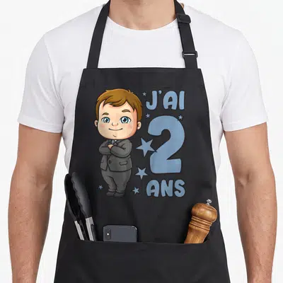 Tablier de cuisine noir avec un dessin d'enfant en costume et l'inscription J'ai 2 ans entourée d'étoiles bleues.