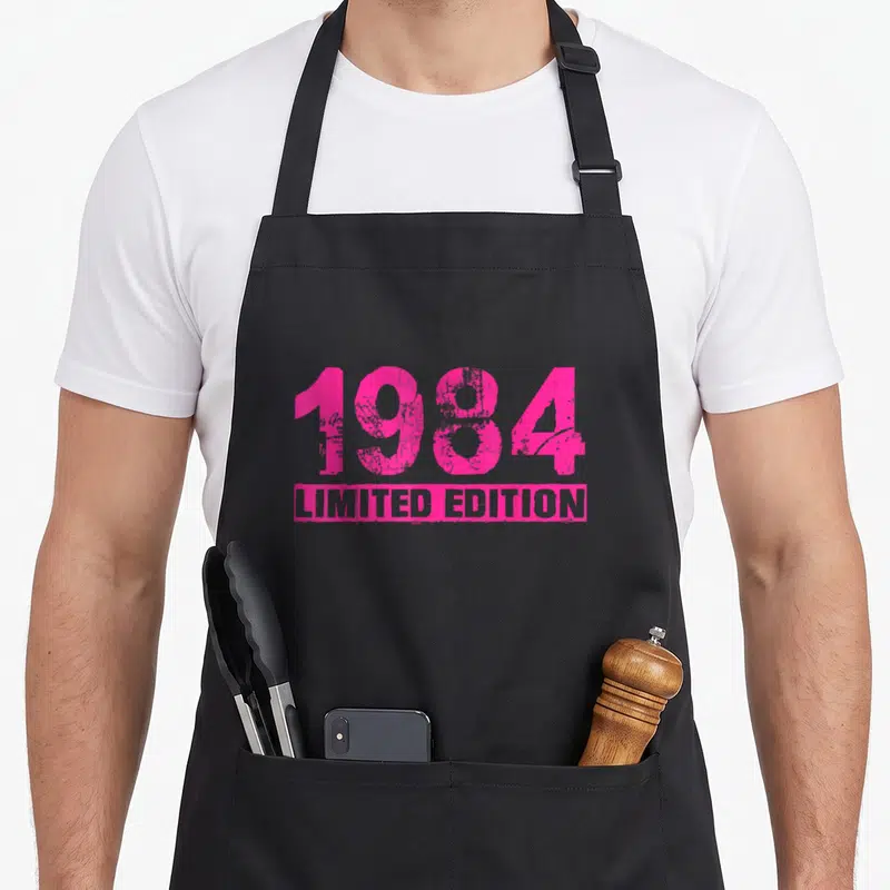 Tablier de cuisine noir avec l'inscription 1984 Limited Edition en rose vif et texture vieillie au centre.