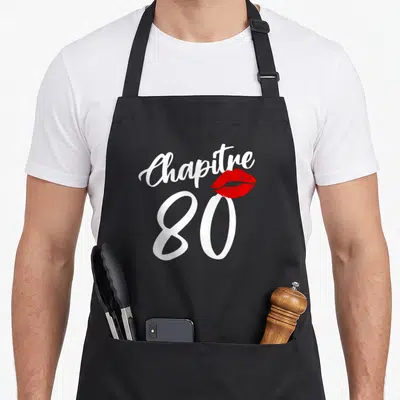 Tablier de cuisine noir avec l'inscription Chapitre 80 et une empreinte de lèvres rouges stylisées au centre du motif imprimé.
