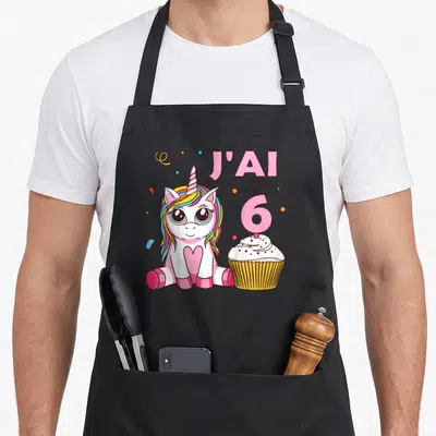 Tablier de cuisine noir avec une licorne rose, un cupcake et le texte J'ai 6 ans imprimé en couleur.