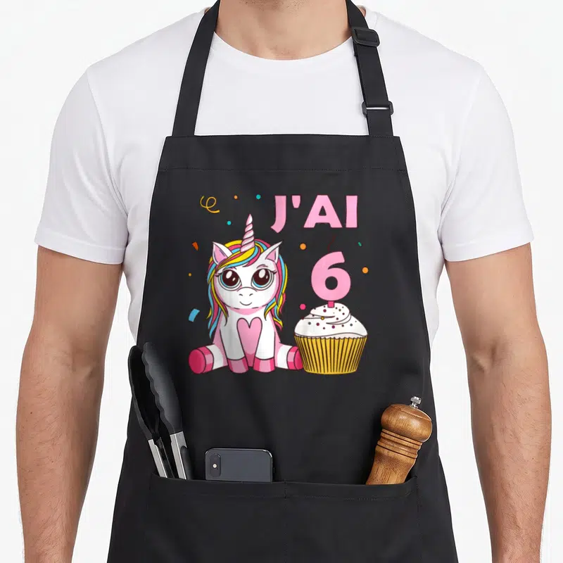 Tablier de cuisine noir avec une licorne rose, un cupcake et le texte J'ai 6 ans imprimé en couleur.