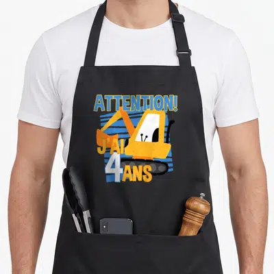Tablier de cuisine noir avec illustration excavateur jaune et texte Attention J'ai 4 ans en bleu et blanc.