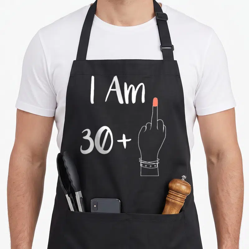 Tablier de cuisine noir avec inscription blanche I Am 30 Plus et main levant un doigt d'honneur au bout rose.