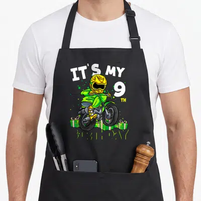 Tablier de cuisine noir avec illustration colorée d'un pilote de moto cross et le texte It's my 9th anniversaire entouré de cadeaux verts.