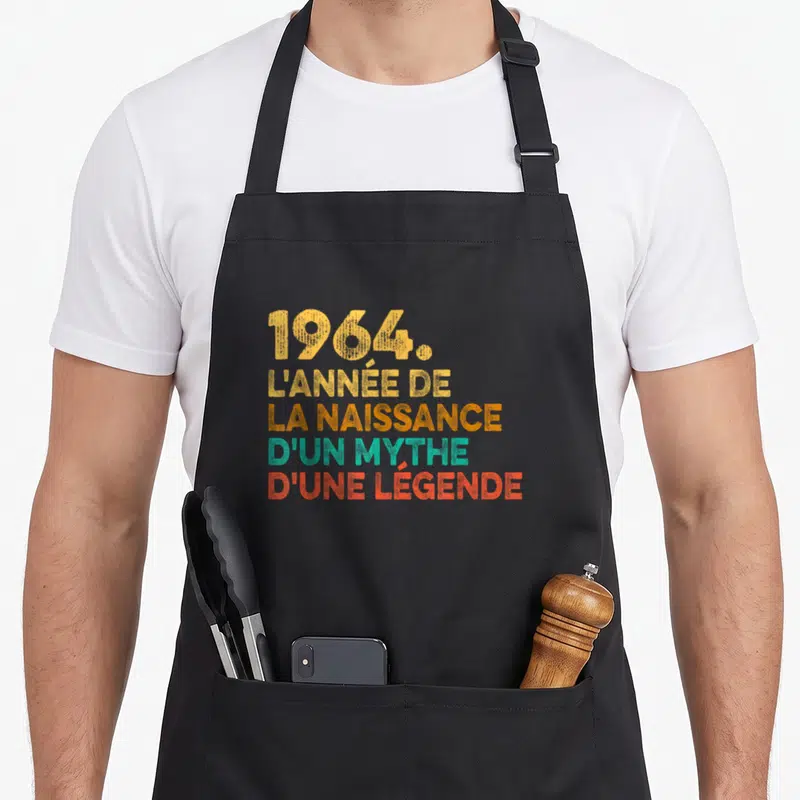 Tablier de cuisine noir avec inscription 1964 l'année de la naissance d'un mythe d'une légende en lettres colorées.