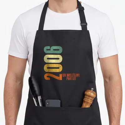 Tablier de cuisine noir avec l'année 2006 imprimée verticalement en couleurs pastel et le texte un millésime parfait en orange.