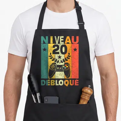 Tablier de cuisine noir avec illustration vintage Niveau 20 Débloqué et manette de jeu vidéo colorée.