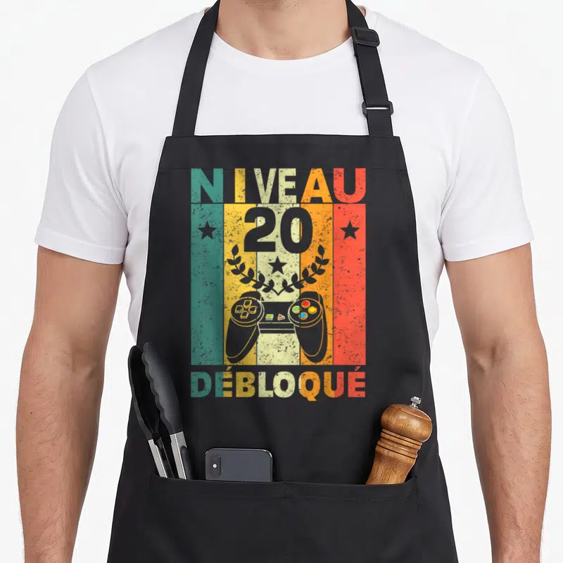 Tablier de cuisine noir avec illustration vintage Niveau 20 Débloqué et manette de jeu vidéo colorée.