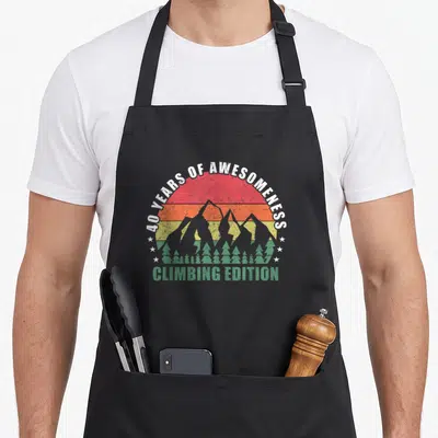 Tablier de cuisine noir avec illustration rétro de montagnes et texte 40 years of awesomeness climbing edition.