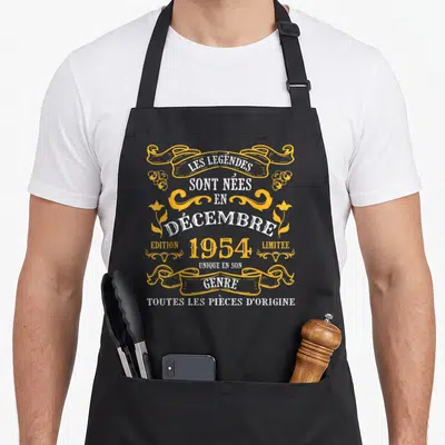 Tablier de cuisine noir avec inscription Les Légendes Sont Nées En Décembre 1954 et détails graphiques dorés sur fond uni.