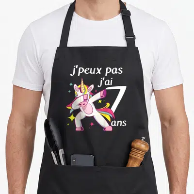 Tablier de cuisine noir avec licorne colorée effectuant un mouvement dab et texte blanc.
