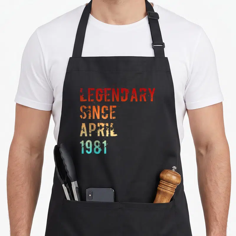 Tablier de cuisine noir avec le texte Legendary Since April 1981 en lettres dégradées orange et bleu turquoise.