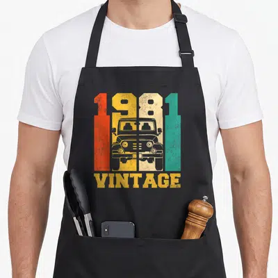 Tablier de cuisine noir avec illustration vintage 1981 4x4 et texte VINTAGE en lettres délavées orange jaune et vert.
