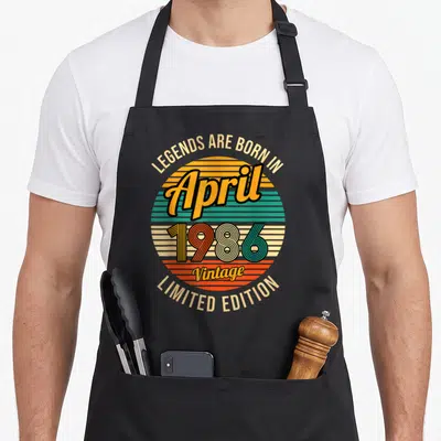 Tablier de cuisine noir avec illustration circulaire retro et texte « April 1986 Limited Edition » au centre.