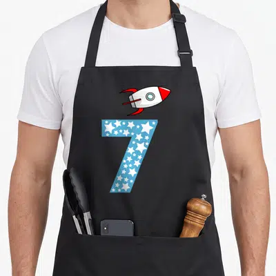 Tablier de cuisine noir avec un chiffre sept bleu rempli d'étoiles et une fusée rouge et blanche au sommet.